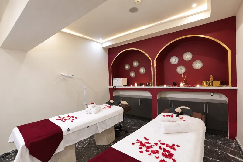 Cabine du spa Orélia à Marrakech, avec deux tables de massage et des arches bordeaux bordées de doré