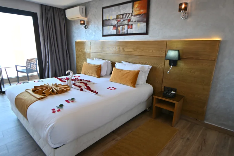 Chambre Deluxe avec grand lit double, coussins ocre et porte-fenêtre donnant sur le balcon