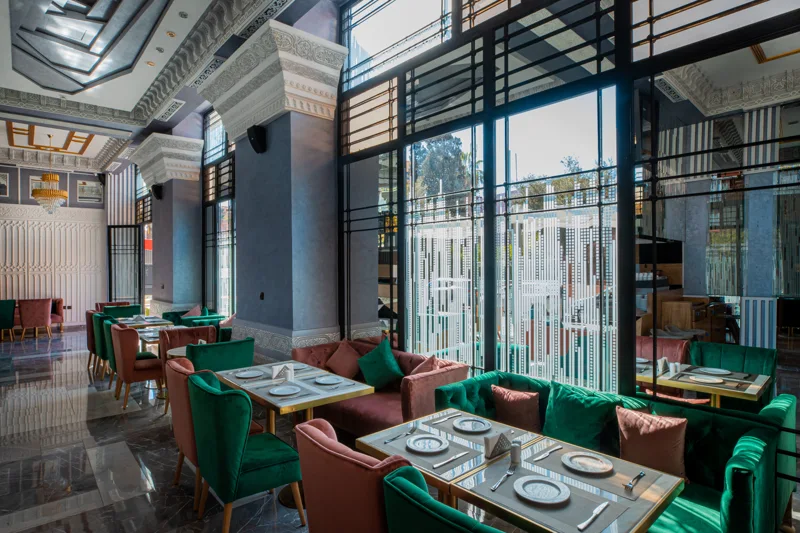 Tables et banquettes vertes du restaurant Pensée à Marrakech, éclairées par les grandes fenêtres