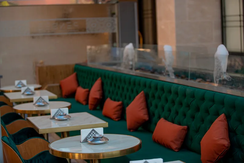 Terrasse du restaurant Pensée à Marrakech, avec banquette verte, tables rondes et fontaines